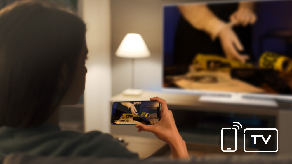 Telewizor JVC LT-32VDF540W - Udostępnianie ekranu telefonu, meżczyzna trzymający smartfon w rękach, na komodzie stojący telewizor, Funkcja współdzielenia ekranu