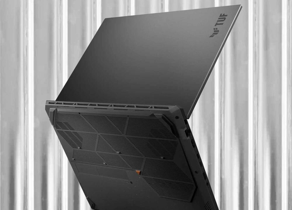 Smukły laptop ASUS TUF Gaming w kolorze szarym, częściowo otwarty, z widocznym logo TUF na pokrywie i zaawansowanym systemem chłodzenia, na tle metalowej ściany. - solidny, lecz bardzo mobilny, Bateria 90 Wh