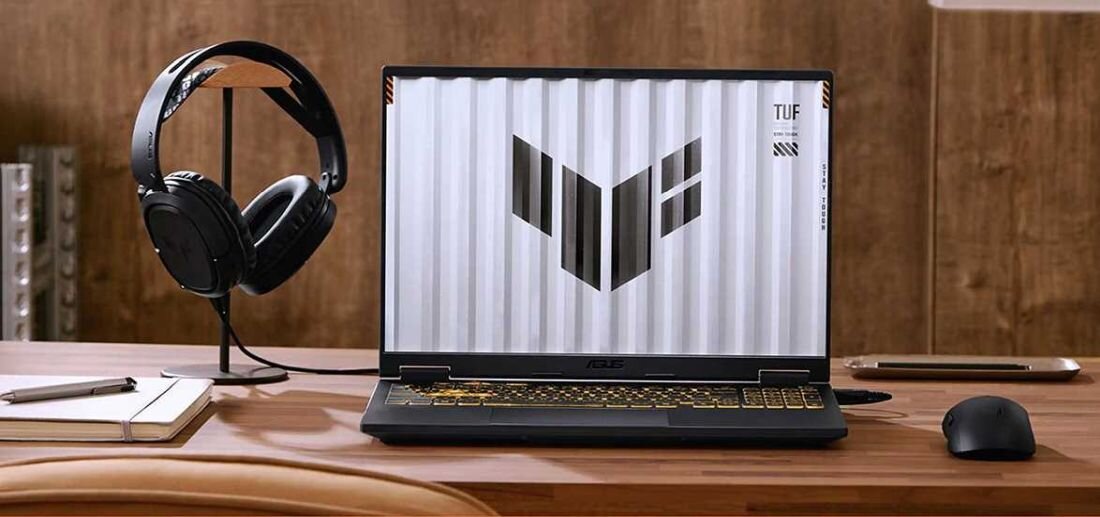Laptop ASUS TUF Gaming z ekranem i logo TUF, podświetlaną klawiaturą RGB na drewnianym biurku, słuchawkami gamingowymi i myszką, stanowisko gracza. - Dwa głośniki z technologią Dolby Atmos