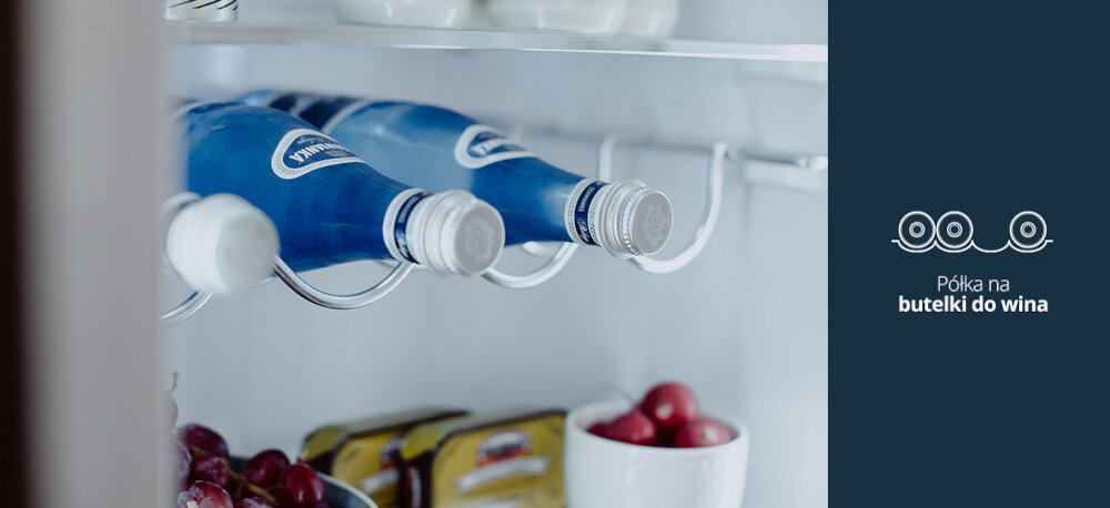 LODÓWKA VESTFROST VR-BF27953H0S Na zdjęciu widać metalową półkę na butelki w lodówce, na której ułożone są poziomo niebieskie butelki napoju. Po prawej stronie, na granatowym tle, znajduje się piktogram butelek oraz napis „Półka na butelki do wina”, podkreślający wygodne przechowywanie wina lub innych napojów w butelkach półka na wino przechowywanie butelek lodówka stylowe wnętrze porządek