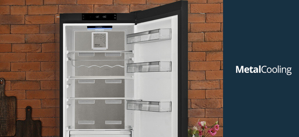 Lodówka VESTFROST VR-FB383-3H0B Na zdjęciu otwarta lodówka Vestfrost z systemem Metal Cooling prezentuje wnętrze wykończone srebrnymi, metalowymi panelami oraz przeźroczystymi półkami na drzwiach. Po prawej stronie, na granatowym tle, widnieje napis „MetalCooling”, podkreślający technologię równomiernego chłodzenia Metal Cooling metalowy panel stabilna temperatura szybkie chłodzenie po otwarciu drzwi energooszczędnoś
