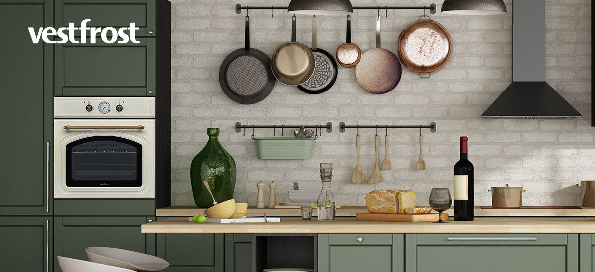 Piekarnik VESTFROST VO-65W19MAVMC Zdjęcie przedstawia stylową kuchnię z zielonymi szafkami, piekarnikiem w zabudowie, wiszącymi patelniami oraz wyeksponowanym chlebem i winem na blacie retro piekarnik do zabudowy beżowy piekarnik