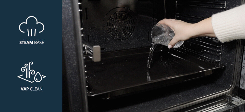 Piekarnik VESTFROST VO-65W19MAVMB Zdjęcie przedstawia wnętrze piekarnika, do którego wlewana jest woda na blachę – to element funkcji Steam Base i Vap Clean. Po lewej stronie widoczne są graficzne oznaczenia tych funkcji, informujące o możliwości pieczenia z dodatkiem pary oraz łatwym czyszczeniu urządzenia przy użyciu pary wodnej steam base vap clean z parą z czyszczeniem parowym z wilgotnym powietrzem łatwy w czyszczeniu para dla smaku