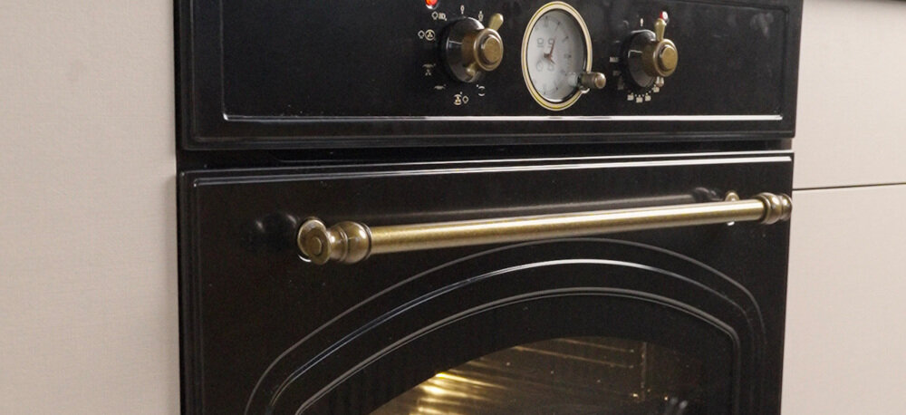 Piekarnik VESTFROST VO-65W19MAVMB Na zdjęciu widoczny jest front piekarnika w stylu retro. Urządzenie posiada masywną mosiężną rączkę, ozdobne pokrętła oraz analogowy zegar podkreślający klasyczny design styl retro matowa czerń chromowane detale retro design do stylowej kuchni vintage