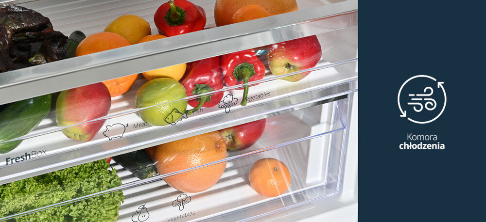 LODÓWKA VESTFROST VR-FB492-3H0B Na zdjęciu widać dolne szuflady lodówki wypełnione świeżymi warzywami i owocami, m.in. papryką, jabłkami, cytrusami i sałatą, oznaczone piktogramami „Meat”, „Fish” i „Vegetables”. Po prawej stronie, na granatowym tle, znajduje się ikona cyrkulacji powietrza z napisem „Komora chłodzenia”, podkreślająca funkcję chłodzącej strefy FreshBox komora niska temperatura mięso ryby sery świeżość bez zamrażania