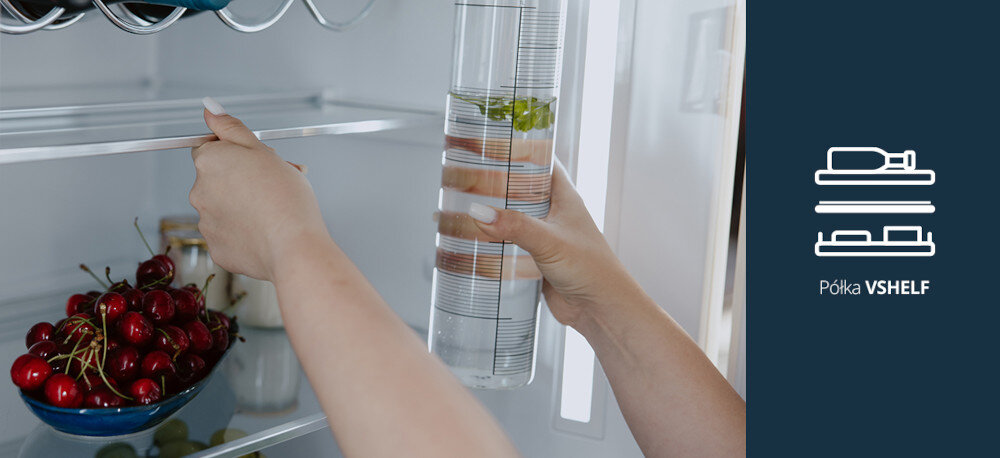 Lodówka VESTFROST VR-FB492-3H0B Na zdjęciu widać wnętrze lodówki, w której jedna ręka wysuwa lub składa szklaną półkę, a druga trzyma wysoki dzbanek z wodą i dodatkami. Na dolnej półce stoi miska z czerwonymi czereśniami, a po prawej, na granatowym tle, znajduje się ikonka dwupoziomowej półki oraz napis „Półka VSHELF”, podkreślający funkcję regulowanej półki vShelf półka teleskopowa składana hartowane szkło regulacja przestrzeni wysokie produkty wygoda