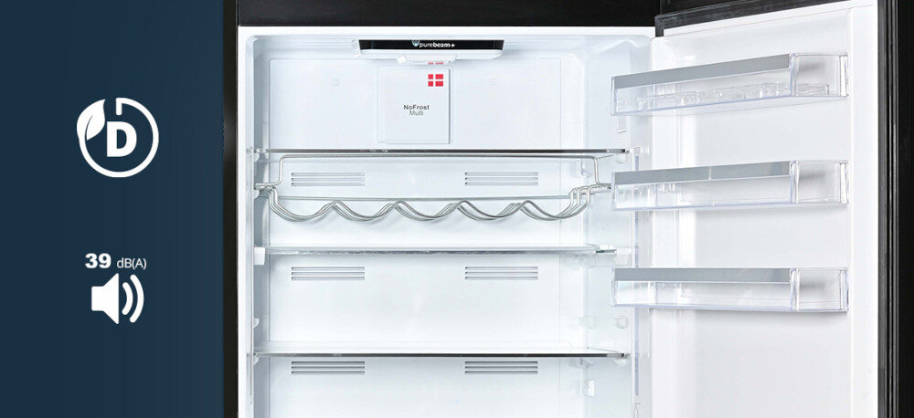 LODÓWKA VESTFROST VR-FB492-3H0B Na zdjęciu pokazano wnętrze lodówki Vestfrost z metalową tylną ścianą, półką na wino i trzema przezroczystymi balkonami na drzwiach. Po lewej stronie, na granatowym tle, widnieje ikona klasy energetycznej z literą „D” oraz symbol głośnika z wartością „39 dB(A)”, informujące o energooszczędności i poziomie hałasu urządzenia Pojemna i energooszczędna