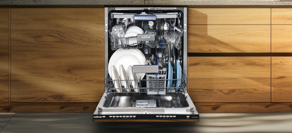 Zmywarka VESTFROST VD-S39B60Q140 Zdjęcie przedstawia w pełni załadowaną zmywarkę Vestfrost w zabudowie drewnianej kuchni, sfotografowaną na wprost z otwartymi drzwiami. Wnętrze urządzenia wypełniają uporządkowane talerze, szklanki, sztućce i akcesoria kuchenne, co podkreśla dużą pojemność i ergonomiczny układ koszy codzienny komfort oszczędność czasu perfekcyjna czystość stylowe rozwiązanie inteligentne mycie nowoczesna kuchnia