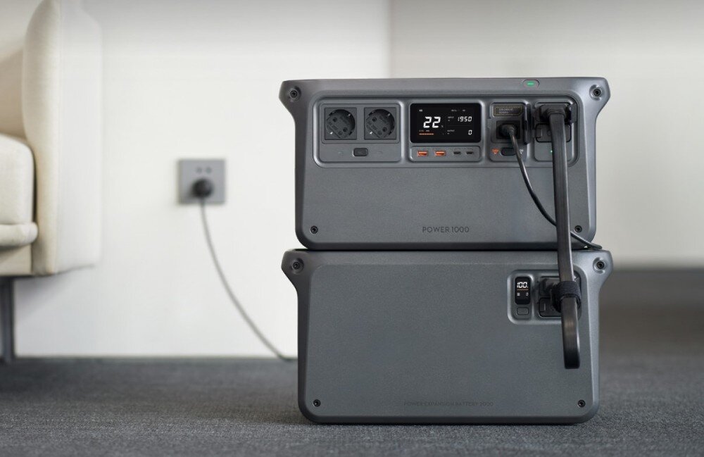 Na obrazie widoczne są dwa szare urządzenia z wyświetlaczem i gniazdami elektrycznymi, ustawione jedno na drugim. Na górnym urządzeniu wyświetlacz pokazuje \'22%\' oraz \'1950\'.