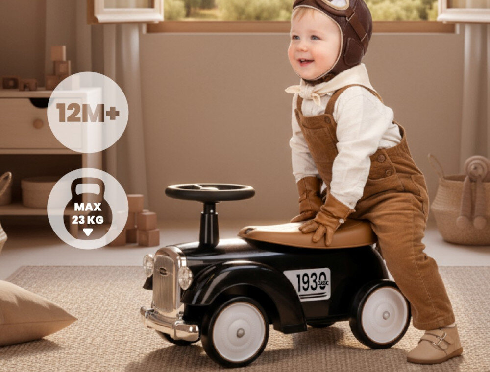 Dziecko siedzi na czarnym jeździku w stylu retro z numerem \'1930\' na boku. Obok widoczne są napisy \'12M+\' i \'MAX 23 KG\'.