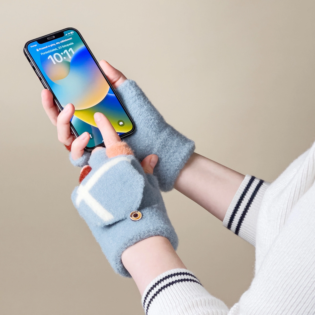 Osoba trzyma smartfon w rękach ubranych w niebieskie rękawiczki zimowe z odkrytymi palcami. Na ekranie telefonu widoczna jest godzina 10:11 i data: poniedziałek, 20 listopada.