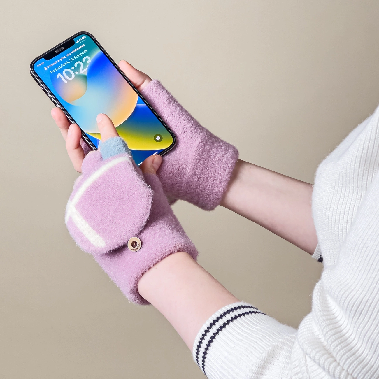 Osoba trzyma smartfon w różowych rękawiczkach z odkrytymi palcami. Na ekranie telefonu widoczna jest godzina 10:22 i data \'Poniedziałek, 28 listopada\'.