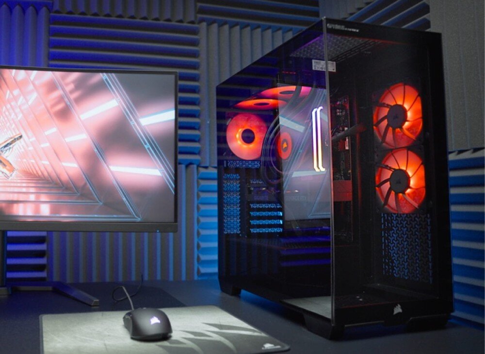 Komputer OPTIMUS E-Sport GB550T-CR7 czarna obudowa z przeszklonym frontem i bokiem stoi na biurku obok monitora wyświetlającego abstrakcyjną grafikę oraz myszki na podkładce, opis