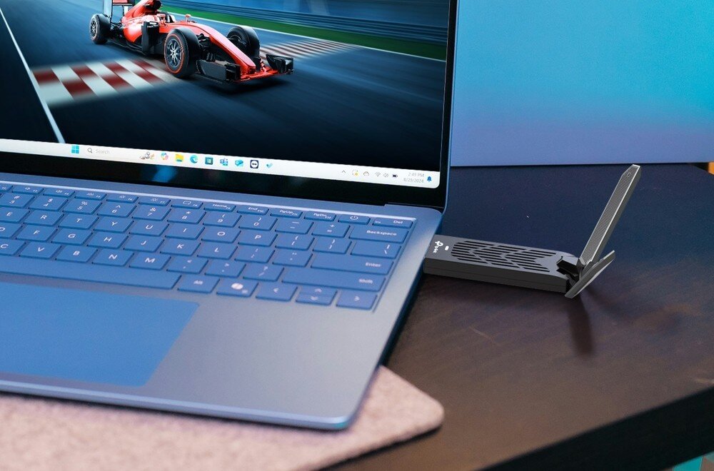 Karta sieciowa TP-LINK Archer TBE400UH Karta sieciowa podłączona do portu USB w laptopie, na którego ekranie widać grę wyścigową, technologie