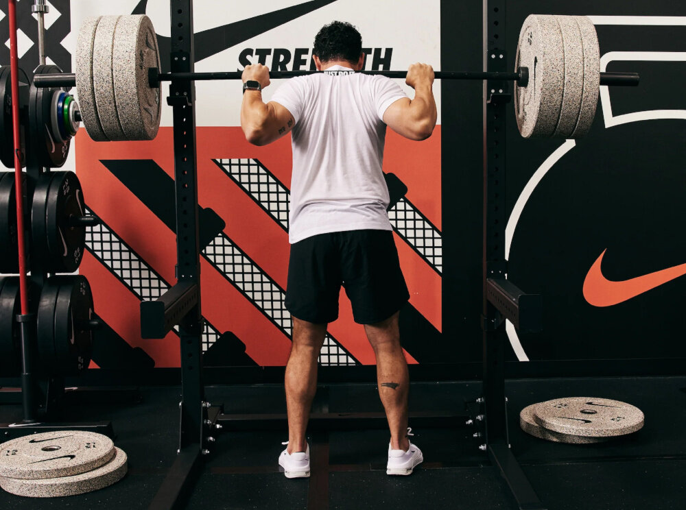 Stojak pod sztangę NIKE Squat Stand sala gimnastyczna osoba ćwiczy ze sztangą przed stojakiem stanowisko do ćwiczeń wszechstronny