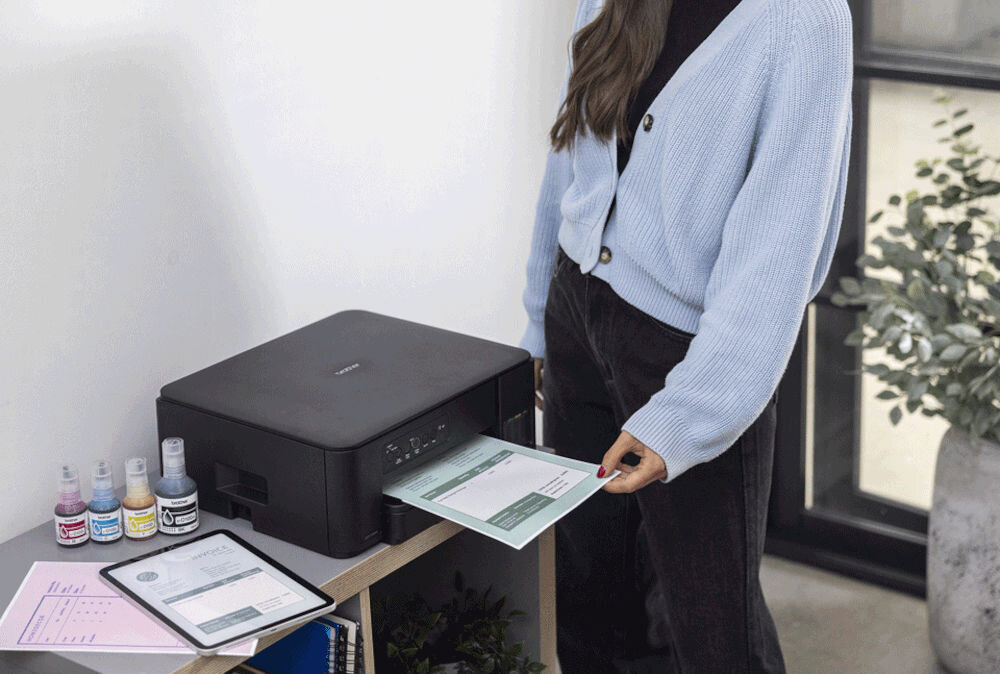 Urządzenie wielofunkcyjne BROTHER DCP-T430W Druk w kolorze, Wi-Fi prezentacja urządzenia w jasnym pokoju na szafce kobieta wyciągająca kartkę
