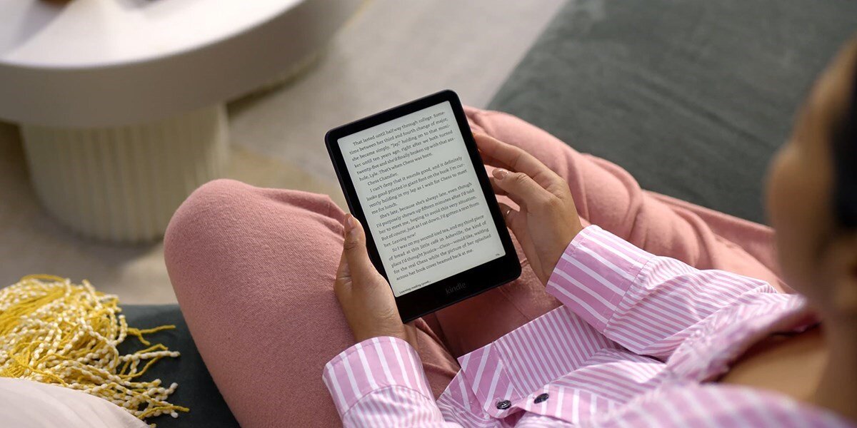Osoba trzyma czytnik e-booków z widocznym tekstem na ekranie. Osoba ubrana jest w różową piżamę w paski.