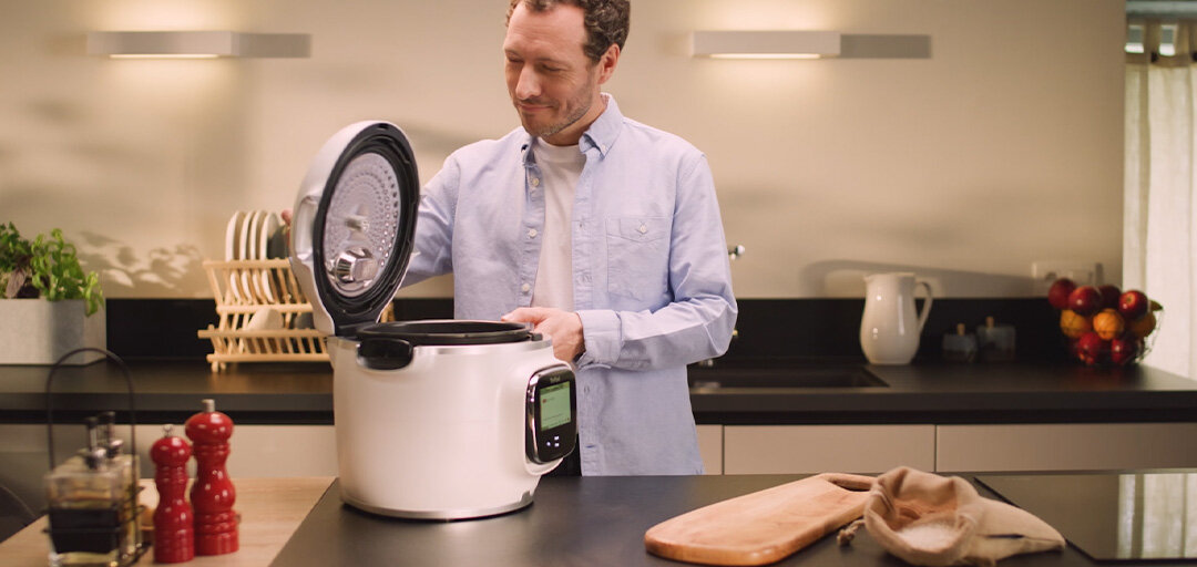 Mężczyzna w kuchni otwiera inteligentny multicooker TEFAL Cook4Me Touch Pro CY94X1F1 na blacie kuchennym.