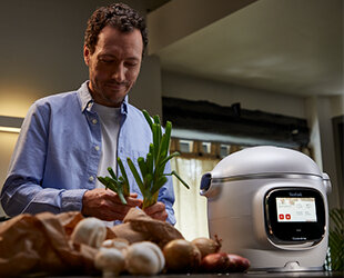 Mężczyzna przygotowuje warzywa obok multicookera TEFAL Cook4Me Touch Pro w nowoczesnej kuchni.