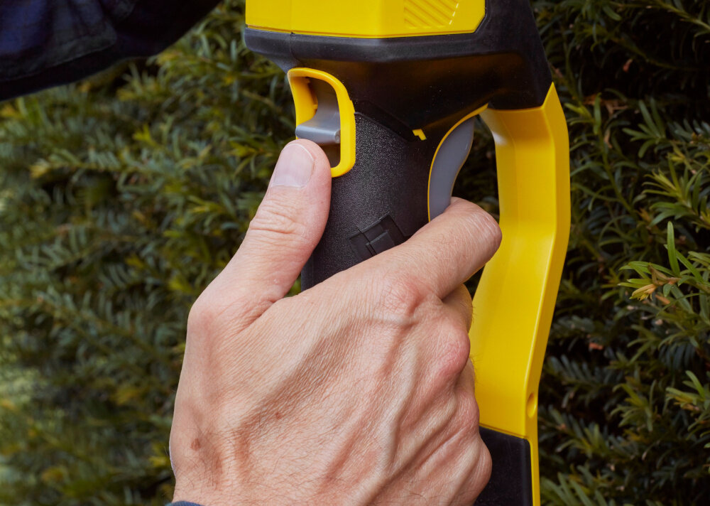 Nożyce do żywopłotu STANLEY Fatmax SFMCPH845B-XJ 450mm 18V akumulatorowe ściana żywopłotu zbliżenia na uchwyt osoba trzyma nożyce w dłoniach waga około 4,1 kg łatwe w prowadzeniu ergonomiczny uchwyt z miękką, antypoślizgową powłoką pewny chwyt i stabilność narzędzia ułatwia precyzyjne cięcie