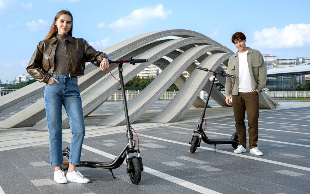 Hulajnoga elektryczna SEGWAY F2 Pro D II 65km 900W 10 cali Czarny miasto dwie osoby stoją obok dwóch hulajnóg w tle abstrakcyjny monument budynki niebo do jazdy po mieście dynamiczne i ekscytujące podróżowanie szereg udogodnień i praktycznych rozwiązań moduł Bluetooth kierunkowskazy składana konstrukcja styl moc wygoda