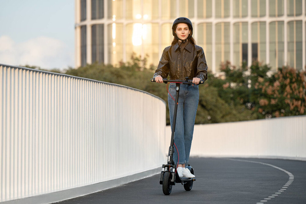 Hulajnoga elektryczna SEGWAY F2 Pro D II 65km 900W 10 cali Czarny miasto budynki osoba jedzie po drodze na hulajnodze niebo rośliny hamulec tarczowy mechaniczny tylny elektryczny bardzo duża siła hamowania wbudowany system TCS system kontroli trakcji utrzymanie większej stabilności podczas jazdy na śliskiej i mokrej drodze