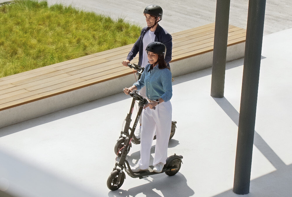 Hulajnoga elektryczna NAVEE V25i Pro 2 20km 300W 10 cali Czarny miasto park droga dwie osoby w kaskach jadą na hulajnogach po drodze środek transportu mobilność styl stabilność