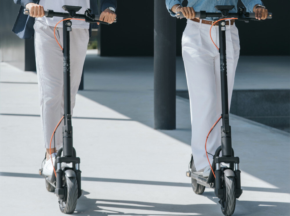 Hulajnoga elektryczna NAVEE V25i Pro 2 20km 300W 10 cali Czarny miasto park droga dwie osoby w kaskach jadą na hulajnogach po drodze wydajna bateria o pojemności 5,1 Ah zasięg do 25 km bateria litowo-jonowa o napięciu 36 V czas ładowania około 4 godzin