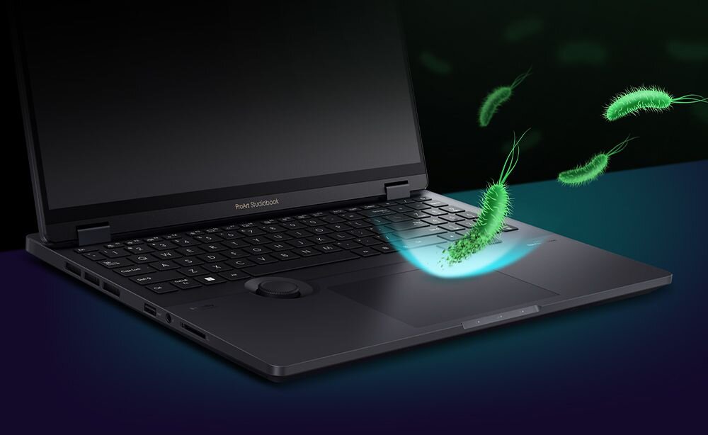  Laptop ASUS ProArt StudioBook z otwartym ekranem na ciemnym tle z zielonymi mikroorganizmami unoszącymi się nad klawiaturą symbolizującymi ochronę antybakteryjną - antybakteryja ASUS 
