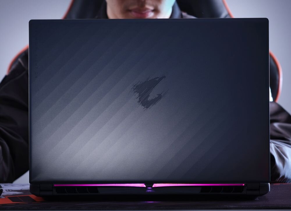 Laptop gamingowy GIGABYTE AORUS stoi na biurku z podświetleniem RGB, podkreślając mocną obudowę stworzoną dla graczy. - Opis serii GIGABYTE Aorus Elite 16   