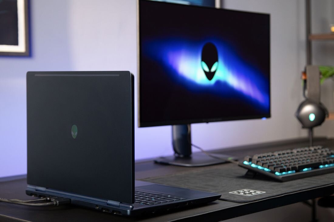 Laptop Alienware podłączony do monitora z logo Alienware, pełnowymiarowa klawiatura i akcesoria gamingowe na biurku - HDMI 2.1 i Thunderbolt 4 USB-A i USB-C