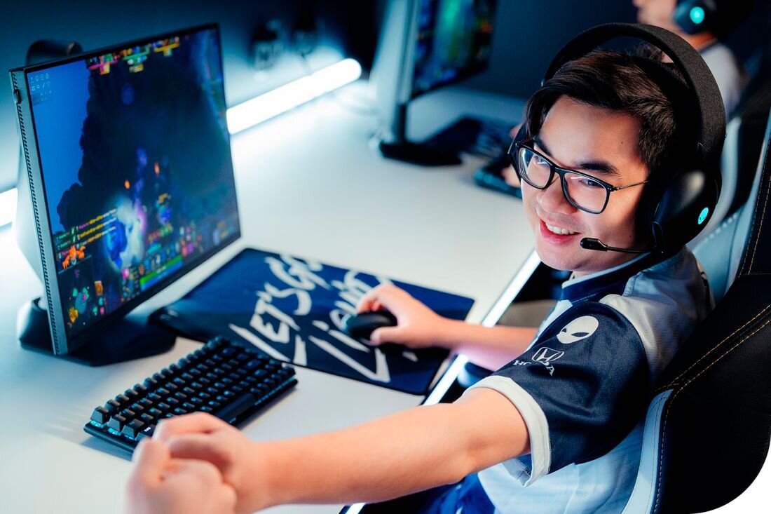  Profesjonalny gracz azjatycki w okularach i słuchawkach gamingowych z Alienware 16 w jasnym studio, gra w kolorową grę na ekranie, klawiatura mechaniczna RGB obok, niebieskie oświetlenie ambientowe, biała mata na biurku, koszulka Team Liquid z logo Honda, pełne stanowisko e-sportowe - Przestrzenny dźwięk w grach Cztery głośniki stereo