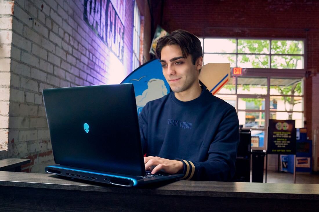 Osoba korzystająca z laptopa Dell Alienware z podświetleniem AlienFX RGB w kawiarni przy stoliku z drewnianym blatem - System podświetlenia AlienFX  