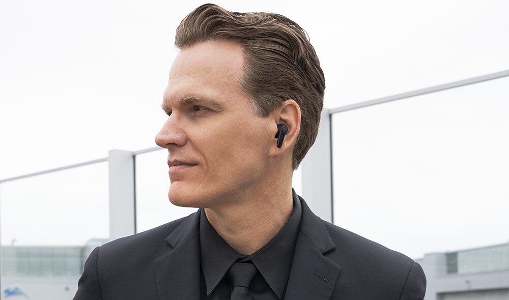 Słuchawki dokanałowe JLAB Jbuds Pods ANC, waga 8,8 g, komfort noszenia, osoba z założonymi słuhcawkami w garniturze na świeżym powietrzu