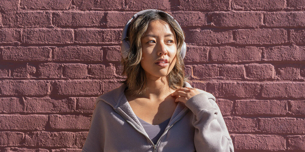 Słuchawki nauszne JLAB GO LUX ANC czas pracy do 70 h akumulator 600 mAh długa bateria, osoba z założonymi słuchawkami na głowie na świeżym powietrzu