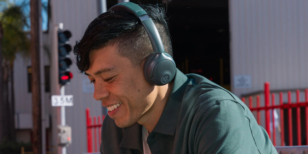 Słuchawki nauszne JLAB GO LUX ANC aktywna redukcja szumów ANC praca w biurze i podróży, osoba z założonymi słuchawkami na głowie na świeżym powietrzu