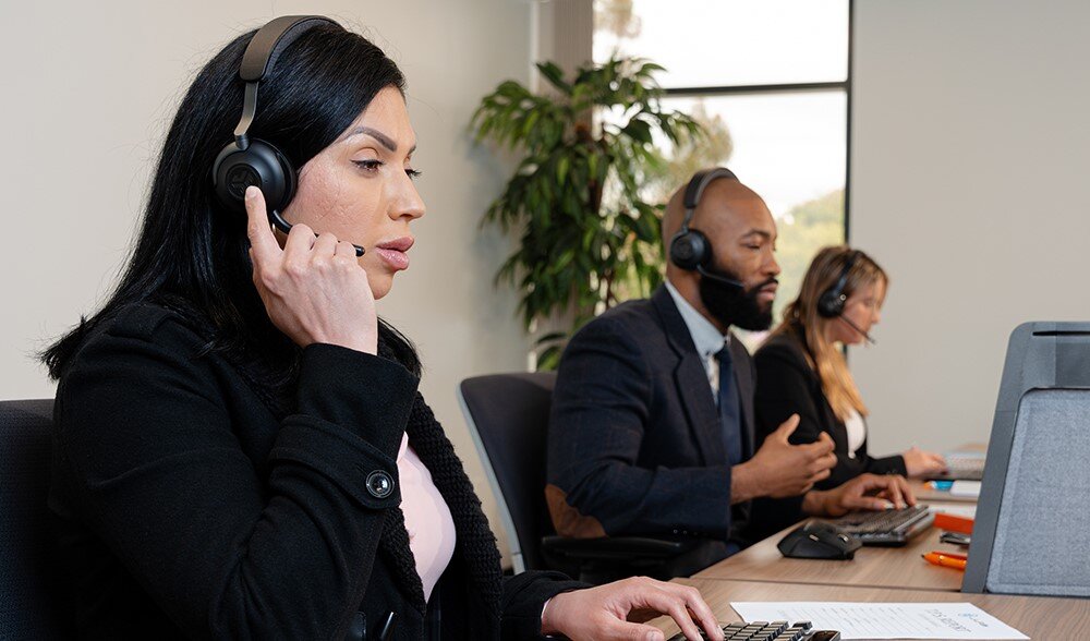 Słuchawki nauszne JLAB Epic Work, wysoka jakość dźwięku, komfort noszenia, osoby siedzące przy biurkach z założonymi słuchawkami nausznymi