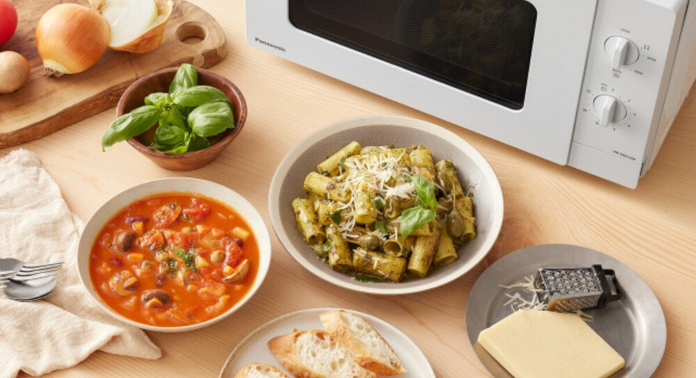 KUCHNIA MIKROFALOWA PANASONIC NN-SM21QWEPG Zbliżenie na blat z potrawami ustawionymi wokół białej kuchenki mikrofalowej Panasonic: talerz makaronu z pesto, miska z zupą warzywną, świeża bazylia, pieczywo oraz ser z tarką, co podkreśla wszechstronne zastosowanie urządzenia do podgrzewania i przygotowywania różnorodnych dań posiłki o każdej porze śniadanie obiad kolacja 5 poziomów mocy 200 W 800 W łatwe rozmrażanie szybkie podgrzewanie przygotowanie dań bez wysiłku