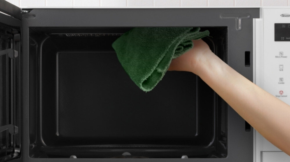 KUCHNIA MIKROFALOWA PANASONIC NN-GD34QWEPG Wnętrze kuchenki mikrofalowej z wyjętym talerzem, czyszczone ręką trzymającą zieloną ściereczkę; grafika podkreśla łatwe, wygodne mycie gładkich ścian komory program Aqua Clean higieniczne czyszczenie łatwe czyszczenie parowe woda z cytryną usuwanie tłuszczu zaschnięte zabrudzenia szybka pielęgnacja wnętrza czystość bez chemii wygoda codziennego użytkowania