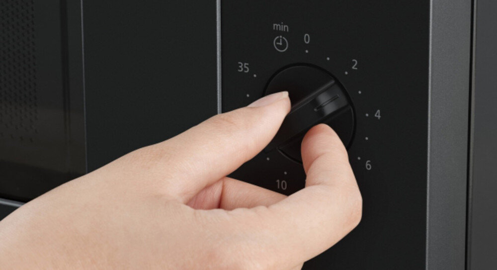 KUCHNIA MIKROFALOWA PANASONIC NN-SM22QBEPG Zbliżenie na panel sterowania czarnej kuchenki mikrofalowej, gdzie dłoń obraca pokrętło minutnika z wyraźną skalą czasu, podkreślając intuicyjną i prostą obsługę urządzenia prosta obsługa szybkie rozpoczęcie gotowania regulacja mocy ustawienie czasu minimalistyczny panel czytelne sterowanie wygodne pokrętła intuicyjna obsługa