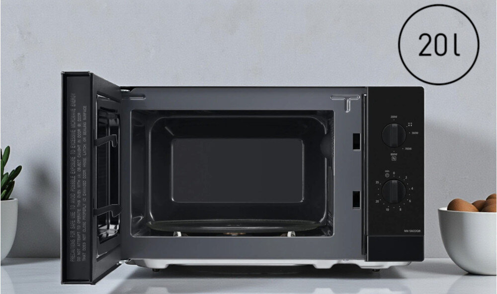 KUCHNIA MIKROFALOWA PANASONIC NN-SM22QBEPG Otwarta Czarna kuchenka mikrofalowa z widoczną komorą o pojemności 20 l i talerzem obrotowym 255 mm, na którym stoi talerz z daniem, pokazuje praktyczną przestrzeń na codzienne posiłki kompaktowe wymiary mała kuchnia pojemność 20 litrów szklany talerz 255 mm większe talerze standardowe naczynia oszczędność miejsca funkcjonalny design