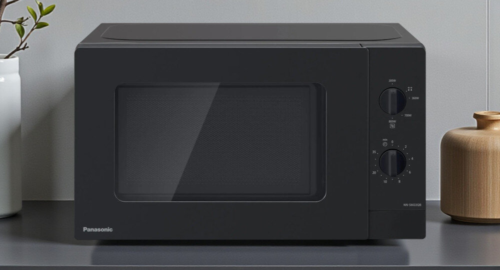 KUCHNIA MIKROFALOWA PANASONIC NN-SM22QBEPG Czarna kuchenka mikrofalowa Panasonic stojąca na blacie w jasnej kuchni, na tle płytek i doniczek z roślinami, eksponuje swój prosty, minimalistyczny design, który łatwo wpasowuje się we wnętrza minimalistyczny design kuchnia zaokrąglone krawędzie czytelne pokrętła matowe wykończenie drzwi estetyczny wygląd codzienny komfort