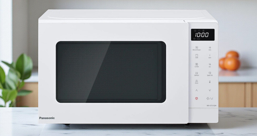 KUCHNIA MIKROFALOWA PANASONIC NN-GT21QWEPG Biała mikrofalówka Panasonic z cyfrowym wyświetlaczem 10:00 i panelem dotykowym po prawej stronie, ustawiona na blacie kuchennym na tle rozmytych owoców i jasnego wnętrza funkcja grilla chrupiące potrawy szybkie gotowanie seria GT kompaktowy design wygląd mała kuchnia łatwa obsługa codzienny komfort grillowanie w domu