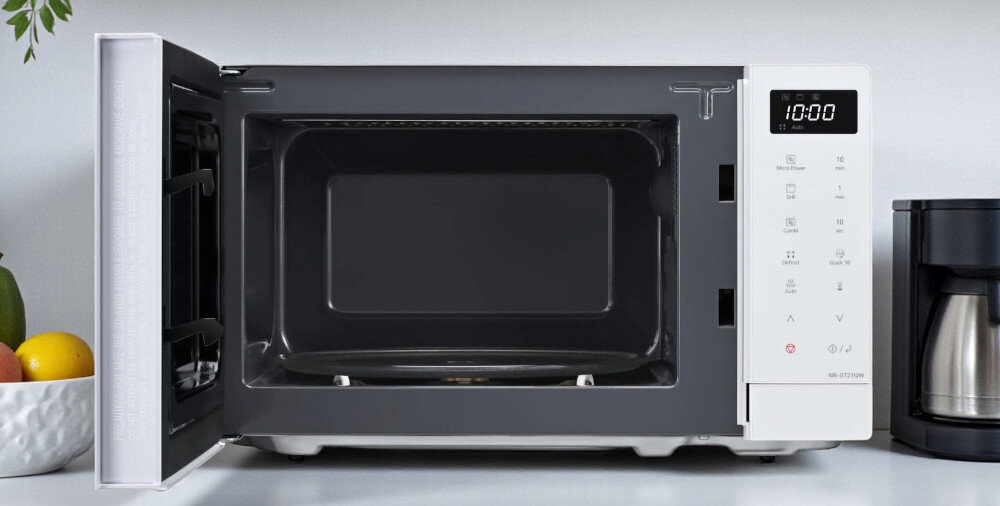 KUCHNIA MIKROFALOWA PANASONIC NN-GT21QWEPG Biała mikrofalówka Panasonic z otwartymi drzwiami, odsłaniająca ciemnoszare wnętrze z talerzem obrotowym; po prawej stronie widać dotykowy panel sterowania z wyświetlaczem 10:00, a obok ekspres do kawy kompaktowe wymiary 440x333x258 mm mała kuchnia pojemność 20 litrów szklany talerz 255 mm większe talerze standardowe naczynia oszczędność miejsca funkcjonalny design praktyczne rozwiązanie