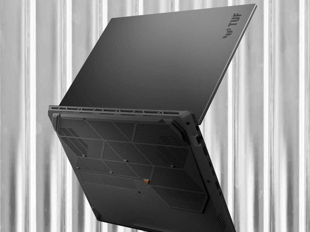Smukły laptop ASUS TUF Gaming w kolorze szarym, częściowo otwarty, z widocznym logo TUF na pokrywie i zaawansowanym systemem chłodzenia, na tle metalowej ściany. - solidny, lecz bardzo mobilny, Bateria 90 Wh