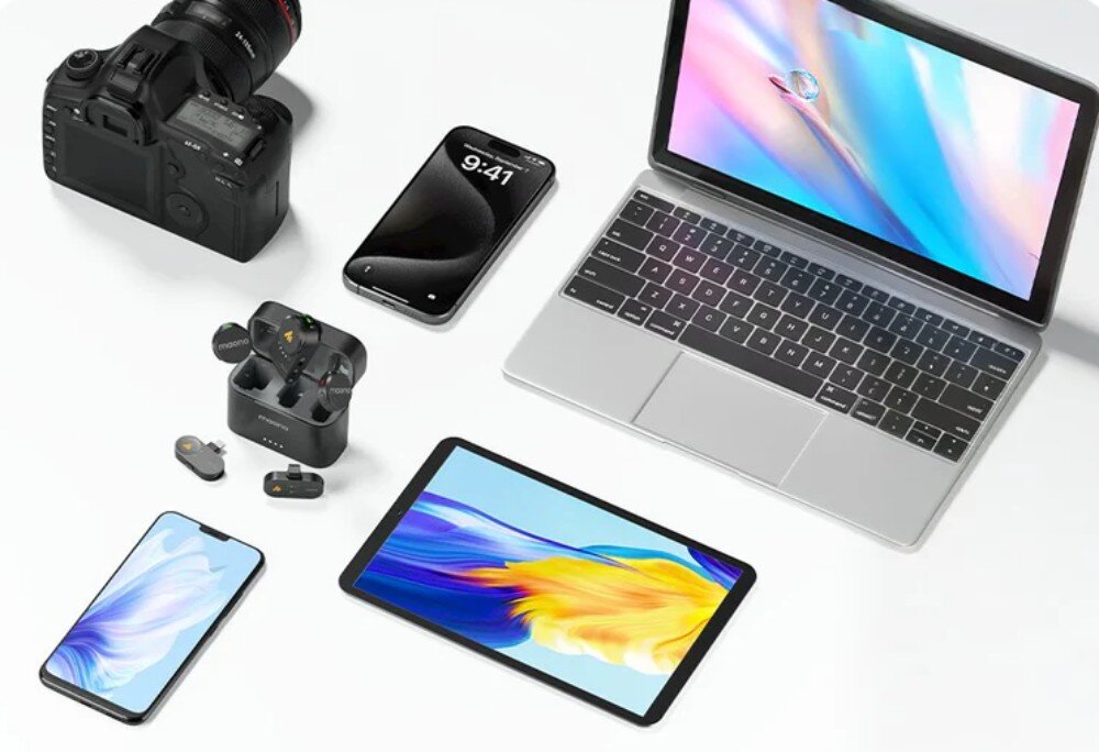 System bezprzewodowy MAONO WM650 A3 Zestaw mikrofonów bezprzewodowych Maono z etui ładującym i dwoma typami odbiorników (Lightning i USB-C) ułożony na białym blacie obok czarnego aparatu DSLR z obiektywem, dwóch smartfonów, srebrnego laptopa i tabletu z kolorowymi ekranami