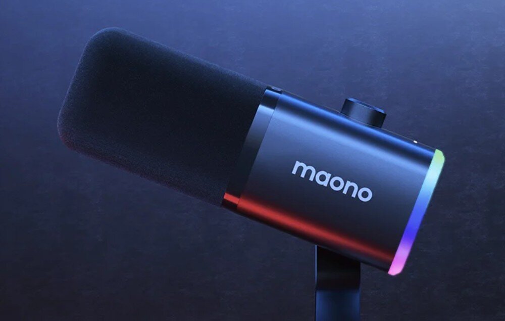 Mikrofon MAONO PD100X Czarny mikrofon o cylindrycznym ksztalcie pokazany z profilu na ciemnym tle. Dolna krawedz obudowy jest podswietlona wielobarwnym swiatlem RGB, a na srodku widnieje bialy napis 'maono'