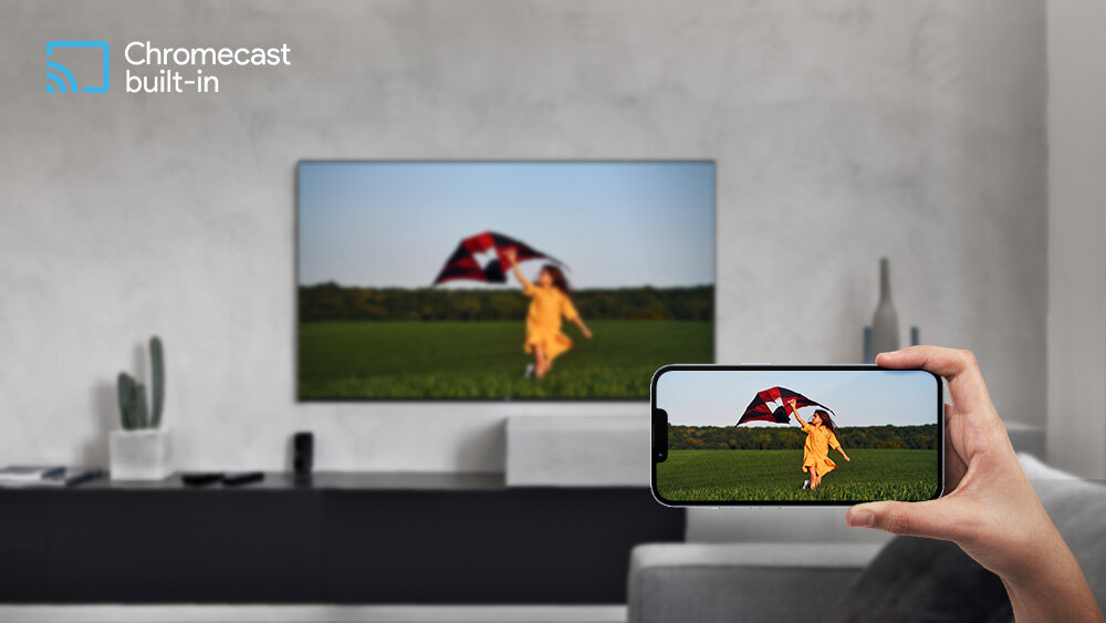 Telewizor JVC LT-40VQF540A - Szybkie wyświetlanie treści, Chromecast, Wi-Fi, telewizor zawieszony na ścianie w pomieszczeniu, ręka trzymająca smartfona