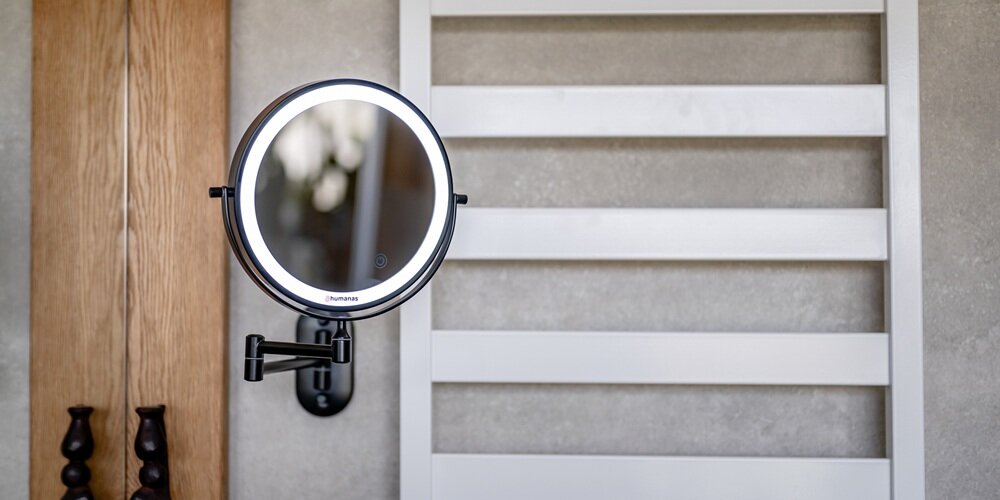 Okrągłe czarne lustro Humanas z podświetlanym pierścieniem, zamontowane na ścianie na przegubowym ramieniu obok kaloryfer