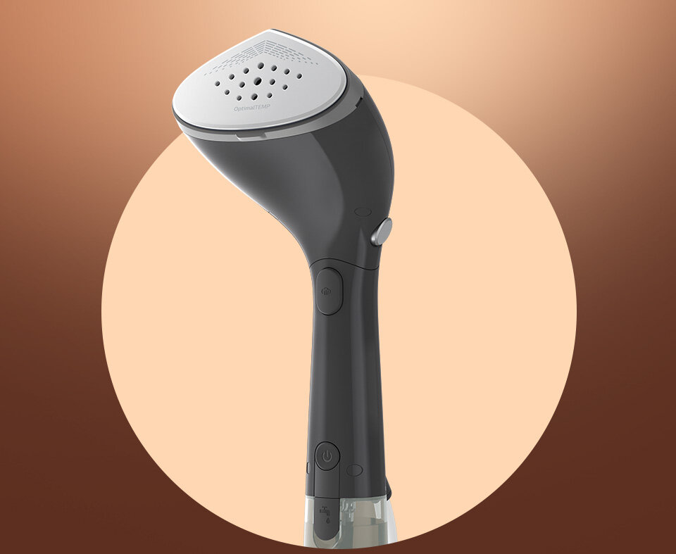 Na obrazie widoczna jest parownica do ubrań w kolorze ciemnoszarym z białą końcówką, na której znajdują się otwory parowe. W tle znajduje się okrągłe, brązowe tło.